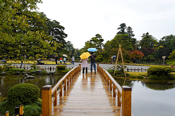 Kanazawa, Japan - November, 11 2010: Japanese people walking on a rainy day over the footbridge and on the footpaths of the beautiful landscaped Kenrokuen Garden in Kanazawa.
