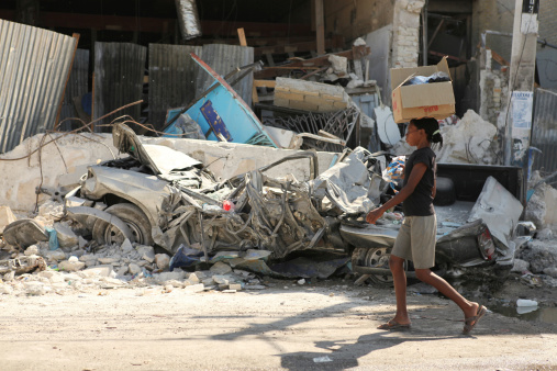 Port-Au-Prince, Haiti - February 4th, 2010 : A young Haitian girl walks past a smashed car and some destroyed buildings without a second glance. After witnessing all the destruction caused by the earthquake, the people of Haiti have grown accustomed to such scenes.