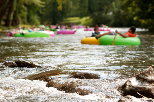 Helen, GA, USA - August 24, 2013:  Defocused people enjoy tubing down the Chattahoochee River in North Georgia on a warm summer afternoon, as river boulders in foreground are in focus.