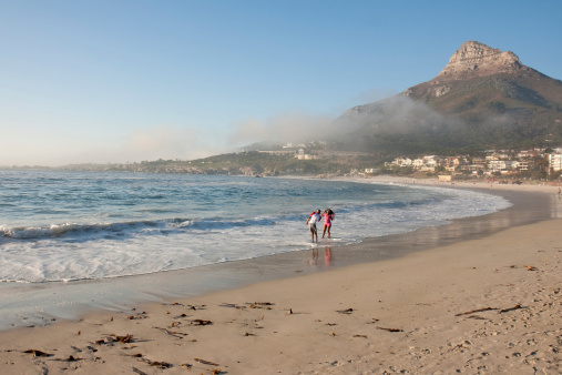 Cape Town, South Africa - March 29, 2011: A woman poses in the surf at Camps Bay beach, Cape Town, for her partner as he takes her picture with a cell phone. Lions Head peak, a Cape Town landmark, is in the background. The beach is a popular attraction for locals and tourists.