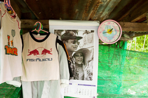 Bangkok, Thailand - June, 23rd 2013: Capture under roof of simple house in Bangkok. In scene is in center a calendar with monochrome photo of King Bhumipol and his wife at younger age. At rigth side is a pink clock. At left side of calendar are some clothes for drying.