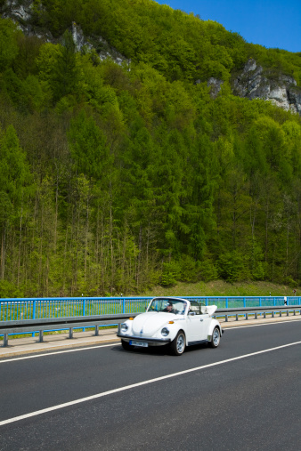 Ebermannschaft, Bavaria, Germany - May, 4th 2008: A couple driving vintage Volkswagen Beetle convertible down the valley in Franconian Switzerland (Fraenkische Schweiz), it is an upland in Upper Franconia, northern Bavaria and a popular tourist retreat, located between the Pegnitz River in the east and the south, the Regnitz River in the west and the Main River in the north, its relief reaches 600 meters in height, the Franconian Switzerland is one of the oldest and most popular holiday areas in Germany, it was given its name by Romantic artists and poets in the 19th century who compared its landscape to Switzerland.
