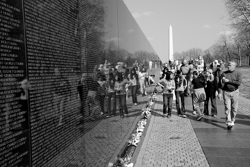 Washington DC, USA - April 10, 2008: At the Vietnam Veterans Memorial, visitors walk alongside the names of the more than 58,000 American military personnel killed during the war in Vietnam. The Washington Monument is in the background