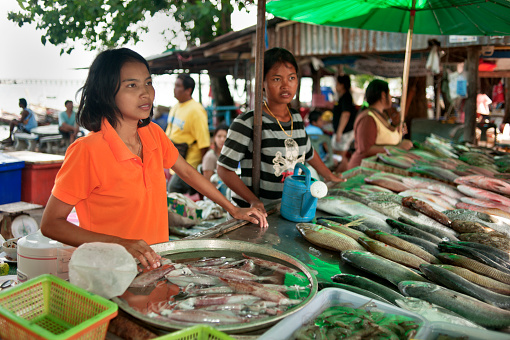 Rawai, Phuket, Thailand - April 26, 2011: A young woman wearing a bright orange shirt selling fish at a street market in Rawai, Phuket, Thailand. This is a sea gypsy market on the edge of a slum area in the south of Phuket.