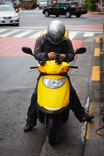 Tokyo, Japan - May 30, 2011: A man driving a Honda scooter stops alongside the street in the Shinjuku district of Tokyo to send a text message on his cellphone. Scooters are a popular method of transportation in Tokyo since they are relatively inexpensive, have good fuel economy and are easy to park.