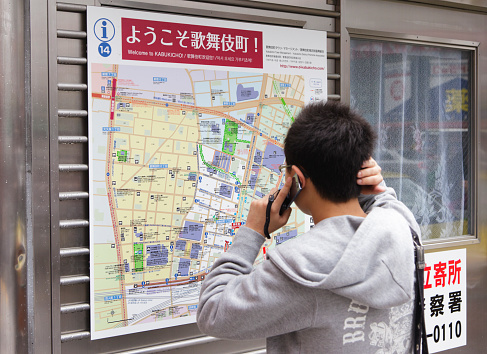 Tokyo, Japan - May 30, 2011: A man reads a map of the Shinjuku area of Tokyo while talking on a cellphone.