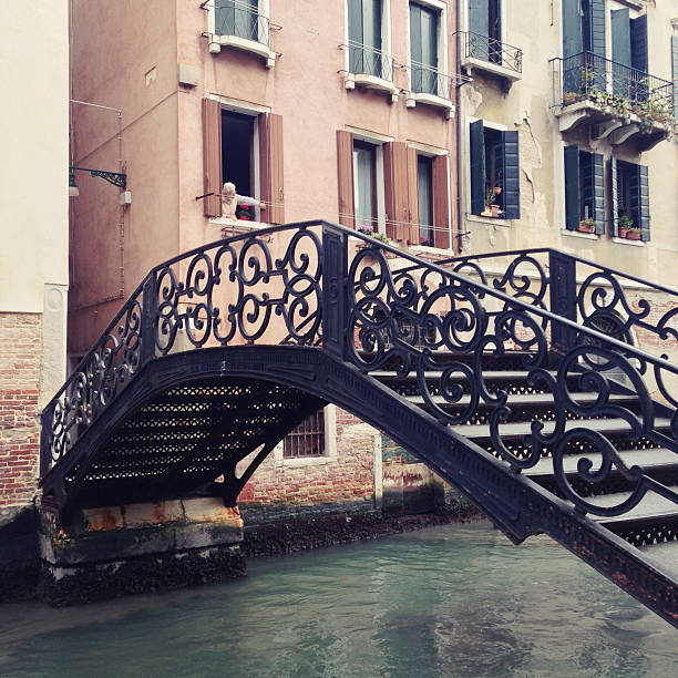 Venezia, Italy - October 3, 2013: despite almost being more a monument than a real town, some people do actually inhabit Venezia. Somebody is opening the window of a house facing one of the canals, surmounted by a beautiful iron bridge.