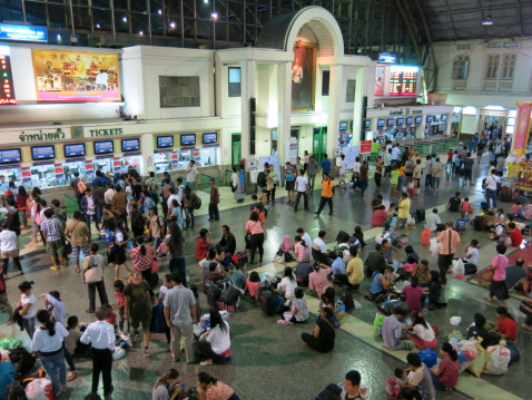Bangkok, Thailand aa October 17, 2013: Thais and tourists queue to buy tickets at Hua Lamphong Railway Station (Bangkok Railway Station), and some sitting on the floor wait for their trains. There is an digital board on the wall showing schedule of trains.  Hua Lamphong Railway Station  is a place where Thais and foreigners take trains to travel in different parts of Thailand.