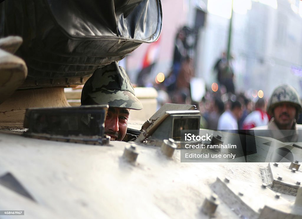 soldier smiling behind a tank Cairo, Egypt - February 1, 2011: over one million Egyptians gather in downtown Cairo - El Tahrir sq (liberation square) to demand political reforms and for the president to step down. The uprising in Egypt started out from social networks on january 25\'th 2011, following a similar successful uprising in Tunis. The picture shows a soldier smiling behind one of the tanks that belong to the Egyptian army after they entered the city to maintain order. Adult Stock Photo