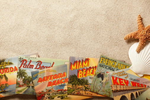 San Diego, California, USA - November 19, 2013: A group of vintage postcards showing various Florida tourist destinations on top of beach sand with starfish and shells. Shot in a studio setting on a tan background.