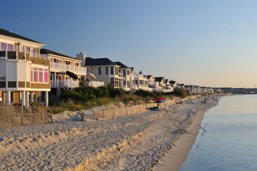 Lewes, Delaware, USA - May 28, 2011. Pristine beach and luxury villa houses with people enjoying beach activities in the background on the Cape Henlopen of Delaware, where thousands of visitors come to enjoy ocean swimming and sunbathing during summertime.