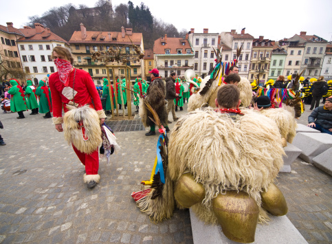 Ljubljana, Slovenia - March 5, 2011: Red kurent with skull resting with group of kurents rest after dancing and jumping, with big bells, which are tied by the waist, are ringing loud. Viewers around them take pictures and laugh. At background is old city of Ljubljana with castle on the hill.