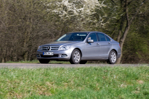 Near Wiesbaden, Germany - April 2, 2011: A senior couple in a silver-metallic Mercedes-Benz C-Class C200 CDI driving on a country-road through the Rheingau (Germany) on a warm spring day. The C-Class-cars (also known as W204-series) are mid-size rear-wheel drive compact executive cars and were launched in 2007. Mercedes-Benz is a German manufacturer of automobiles and trucks and a division of Daimler AG, formerly Daimler-Chrysler. Some motion blur