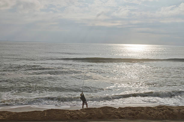 Cape Hatteras, North Carolina, USA - October 18, 2013: Fisherman stands on the beach with his fishing pole and casts a line into the ocean