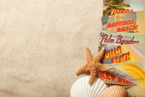 San Diego, California, USA - November 19, 2013: A group of vintage postcards showing various Florida tourist destinations on top of beach sand with starfish and shells. Shot in a studio setting on a tan background.