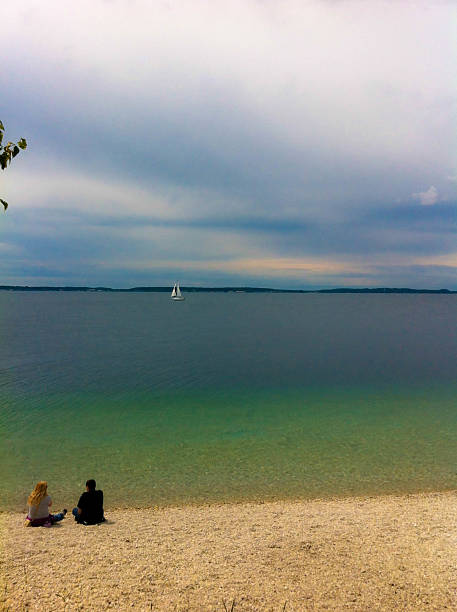 Michigan, United States - August 5, 2013: A couple of people sitting on the shore of Mackinaw Island Michigan, watching a sailboat in the distance.