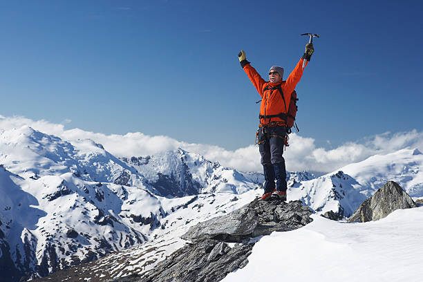 Mountain Climber With Arms Raised On Snowy Peak Male mountain climber raising hands with icepick on top of snowy peak snow hiking stock pictures, royalty-free photos & images