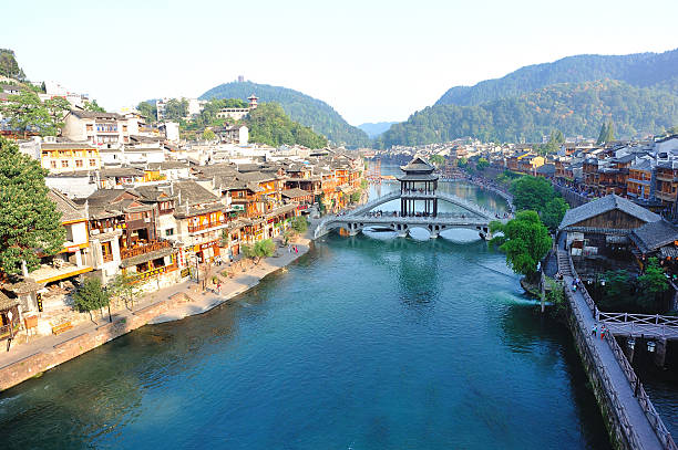 Fenghuang, A!hina - October 12, 2013: Woodens houses and bridge with toujiang river in fenghuang ancient town,dozens of tourist walking on the shore,many tourist walking/standing in the distance,fenghuang county,hunan province,china
