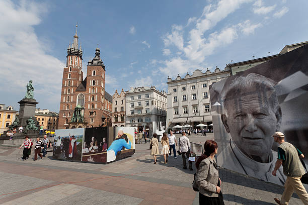 John Paul II Krakow, Poland - April 23, 2011:Preparations for the coming  beatification of Pope John Paul II on 1 May which will  officially take place in Rome.Big photographs of the Pope are exposed on the Main Market Square of Krakow.Some of the passers-by are watching the photographs.Behind is the Mariacki church and Adam Mickiewicz monument. pope john paul ii stock pictures, royalty-free photos & images