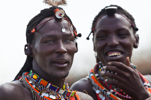 Masai Mara, Kenya - September 16, 2010: Two young Masai warriors are seen in their ceremonial dress. They are sharing a laugh while meeting visitors to their village where they demonstrate traditional culture. They are in the Masai Mara region of southwestern Kenya.