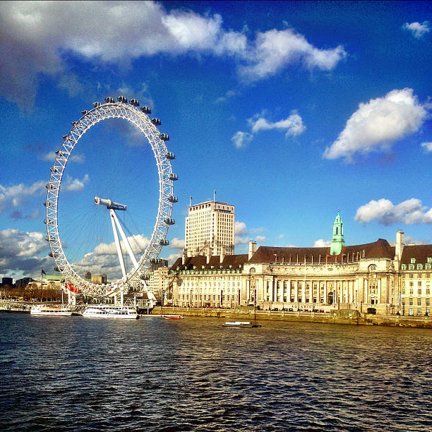 London Eye and County Hall London, UK - 18 April, 2013: A sunny view of the popular London landmark, The London Eye, next to the former County Hall building which now houses various tourist attractions.  Tourists and pleasure boats visible in the foreground on the banks of the River Thames. london county hall stock pictures, royalty-free photos & images