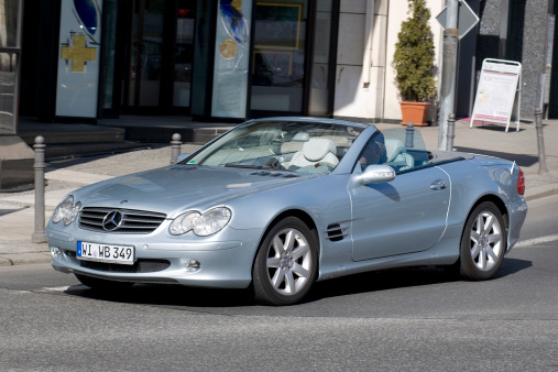 Wiesbaden, Germany - April 7, 2011: A senior man in a blueish metallic Mercedes-Benz SL-Class convertible (R230-Series) turning right on a street corner in Wiesbaden on a sunny spring morning. Mercedes-Benz SL-Class cars (also known as R230-Series) are luxury roadster cars produced by the German car manufacturer Mercedes-Benz. The first generation was introduced in 1954 with the famous 300 SL &amp;amp;quot;gullwing&amp;amp;quot;. Mercedes-Benz is a German manufacturer of automobiles and trucks and a division of Daimler AG, formerly Daimler-Chrysler. Some minor motion blur.