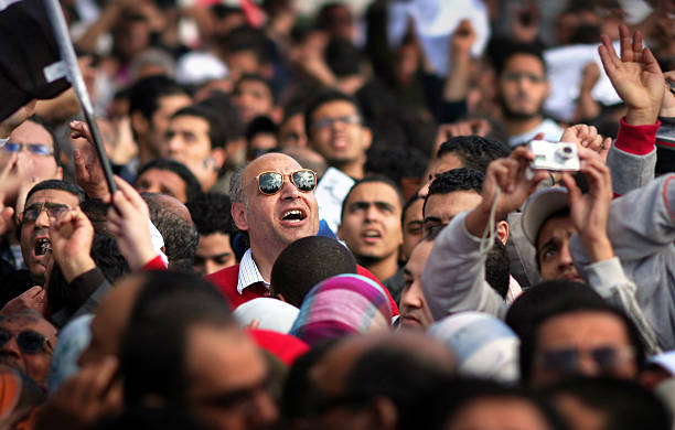 protesters watching a military helicopter fly low above liberation square stock photo