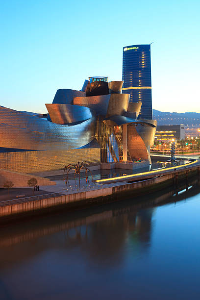 Guggenheim Museum Bilbao and Iberdrola tower Bilbao, Spain - March 31, 2011: View of Guggenheim Museum Bilbao, designed by the architect Frank Gehry, reflected in Nervion River during dusk and Iberdrola Tower, designed by Cesar Pelli. The museum is a mayor tourist attraction in Bilbao and an architectural milestone of the last century and the skyscraper is the new headquarters of the basque utilities company Iberdrola. frank gehry building stock pictures, royalty-free photos & images