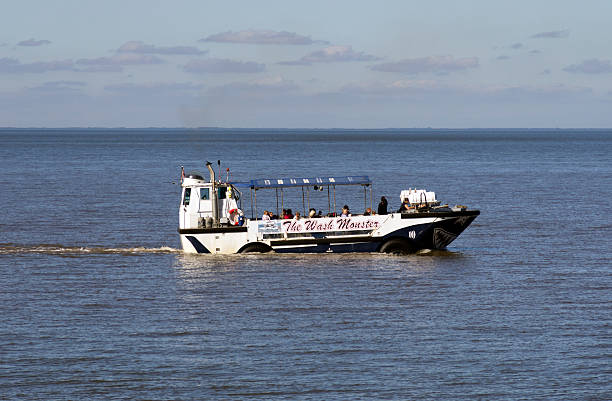 Hunstanton, England - September 22, 2013: Holidaymakers travelling in aEThe Wash Monsteraa at Hunstanton in West Norfolk, England. aEWiley The Wash Monsteraa is an amphibious vehicle which operates tours along this coast  to see the famous striped cliffs and seal colonies and is an old US amphibious craft which was originally used for landing troops on the beaches of Vietnam during the Vietnam War. The coast of Lincolnshire can be seen across The Wash. (Bright sunlight.)