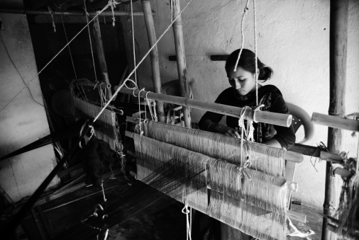 Gorkha, Nepal - November 1, 2010: A girl weaving Dhaka by Handloom. Dhaka is a popular pattern and style of cloth, famous in Nepal which is synonymous to Nepalese people. It is often related with National identity.