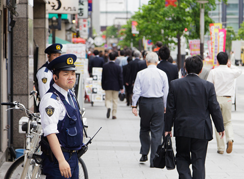 Tokyo, Japan - May 31, 2011: Two uniformed police officers from the Tokyo Metropolitan Police Department monitor the foot traffic on a sidewalk in the Hamamatsucho business district of Minato Ward in Tokyo.