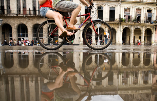 Havana, Cuba - September 16, 2010: A young Cuban couple cycle through the water on the wet streets of Havana. In the background are buildings with beautiful, classic Cuban architecture.
