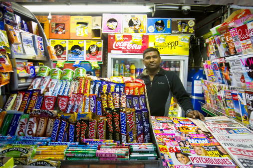 London, United Kingdom: May 3, 2011 - Vijay Patel. standing in his small shop in the Embankment Underground station. Small shops like this are everywhere in London catering for the needs of people on the move. High iso image.