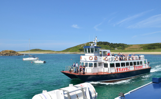 Channel Islands, UK - July 5, 2013: A small passanger ferry passes on the way to Herm Island, part of the Channel Islands. Logos and many people of various ages in shot. Other boats in the background.