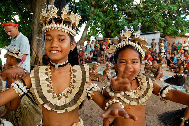 Two school children performing traditional dance Tabiang Village, Fiji Islands - June, 22 2007: Local schoolgirls perform a dance depicting their peoples flight to a new island home from Ocean Island after persecution by the British Phosphate Company in the late 1800\'s. In the background enjoying the performance are school teachers,  an eco-tourist and village children. The school buildings can also be seen in the background. The school is always seeking donations improve its infrastructure. fiji stock pictures, royalty-free photos & images