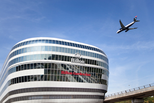 Frankfurt, Germany - August 15, 2013: Facade of The Squaire with the logos of Hilton and Hilton Garden Inn. The Squaire is a large office and hotel building complex which is built on top of an existing train station as a part of the Frankfurt International Airport. It is connected to Terminal 1 via a skyway. In the background a landing airplane