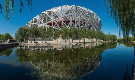 Beijing, China - 25th September 2013: The iconic steel lattice of Beijing's National Stadium, or Bird's Nest, reflecting in the tranquil waters of Olympic Park lake in the heart of China's vibrant capital city. Composite panoramic image created from six contemporaneous sequential photographs.