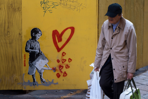 Bologna, Italy - October 16, 2013: An old man passes by a street graffiti of a boy with a water bucket with hearts coming out from it.
