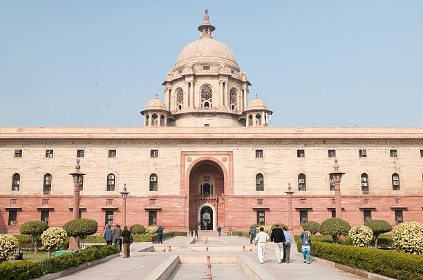New Delhi, India - December 31, 2010: Front entrance of the Indian Parliament building. People are walking towards the entrance. The Indian Parliament has two houses - Lok Sabha and Rajya Sabha. The inscription on the entrance seen here reads \