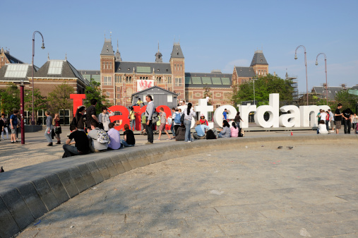 Amsterdam, the Netherlands - April 21, 2011: Large public sculpture &amp;quot;I Amsterdam&amp;quot; letters in front of Rijksmuseum Amsterdam. &amp;quot;I Amsterdam&amp;quot; is the city's current motto and marketing slogan. The letters travel throughout the city. Lots of tourists have their picture taken in front or on top of the letters. The letters are on Museumplein (English: Museum Square). At the forefront you can see part of a (usually fully filled) shallow pond.Rijksmuseum (English: State Museum) Amsterdam at the background is being restored and renovated since 2003. It will reopen in 2013. A 400 piece top collection is still on display, in an already renovated part of the museum. Two of the most famous paintings in Rijksmuseum are 'The Night Watch' by Rembrandt van Rijn, and 'The Milkmaid' by Johannes Vermeer. Besides Rijksmuseum, three other museums are located around the square: the Van Gogh Museum, the Stedelijk Museum and the Diamond Museum.