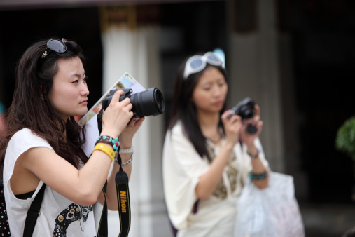 Bangkok, Thailand - March 27, 2011: Two pretty young Asian photographers take pictures. They are in summer clothes at the Grand Palace in Bangkok. In the foreground, a young woman prepares to take a picture and the background, another young woman makes adjustments to his camera