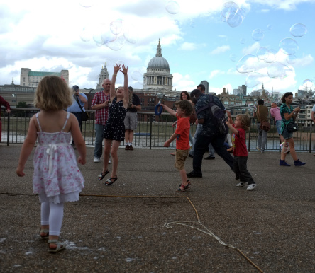 London, England - July 28,2013: Kids try to catch floating bubbles on the South Bank of the River Thames in London.