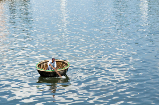 Phan Thiet, Vietnam - November, 17 2006: A man paddling a small round boat in Phan Thiet Harbour. Phan Thiet is a small town in Southern Vietnam. The town has a large fishing industry and is also a stopping off point for many tourist traveling to the near by beach resort of Mui Ne