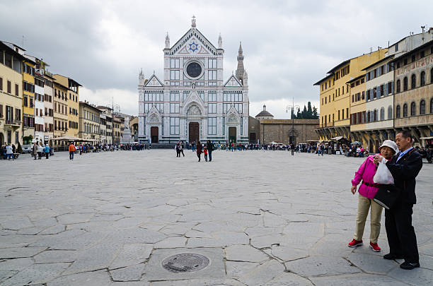Florence, Italy - April 20, 2013: tourists in Santa Croce square. In the foreground, two Chinese tourists looking at their camera. Cloudy day.
