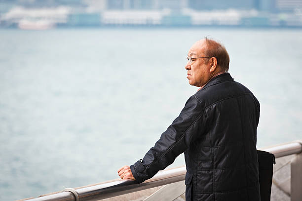 Hong Kong, China - January 16th, 2011: Senior Chinese man looking out over Hong Kong Harbour from the Avenue of Stars on the Tsim Sha Tsui waterfront towards the crowded skyscraper cityscape of Hong Kong Island\\'s Central District.