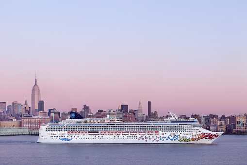 New York City, USA - December 18th, 2011: A Norwegian cruise ship departs on the Hudson River during dusk, passing Manhattan in the background. 