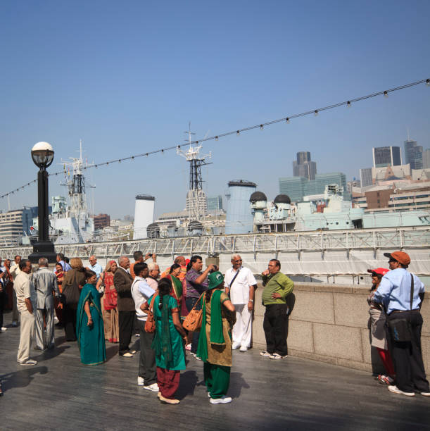 London, United Kingdom - April 20, 2011: A group of Indian Tourists are posing in front of the HMS Belfast on the sourthern bank of the river Thames in London. They are taking photographs with the Tower Bridge as a background.