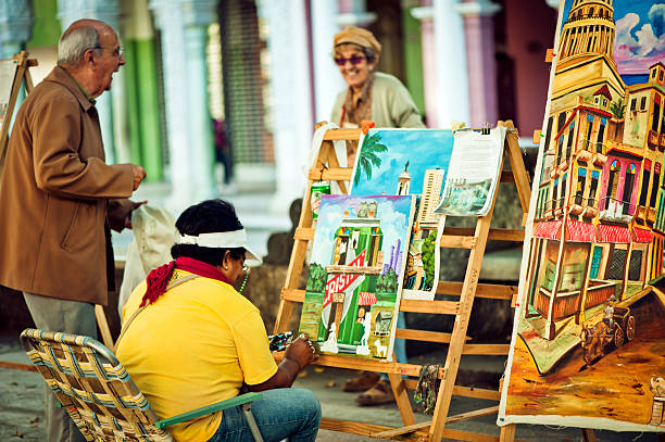 Havana, Cuba - January 3, 2011: Female artist painting right at Prado street in Havana and Cuban senior man and woman talking near her.