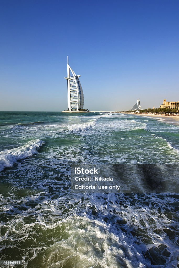 The Burj Al Arab Hotel in Dubai Dubai, United Arab Emirates - February 21, 2010: The Burj Al Arab Hotel, left side on the beach near Madinat Jumeriah Resort. The Burj Al Arab is a luxury hotel located in Dubai, United Arab Emirates. At 321 m (1,053 ft), it is the fourth tallest hotel in the world. The Burj Al Arab stands on an artificial island 280 m (920 ft) out from Jumeirah beach, and is connected to the mainland by a private curving bridge. It is an iconic structure whose shape mimics the sail of a ship. Beach Stock Photo