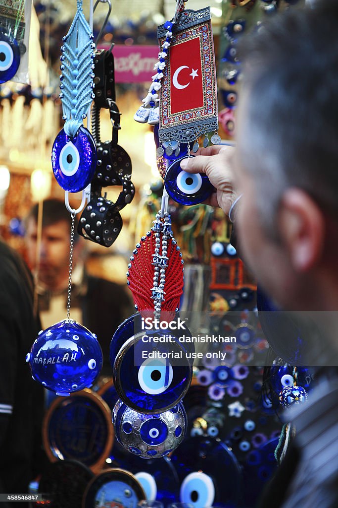 Nazar Boncuk Good luck Eye Istanbul, Turkey - November 6, 2009: Tourist is buying evil eye souvenir, from Misir Carsisi. In Turkey, wherever you look, you'll meet plenty of eyes looking at you. It is common in the Turkish culture to give a gift of a Blue Glass Nazar Boncugu (Nazar boncuk) or The Evil Eye Bead as it is more widely known.  People hang a small evil eye amulet from the rear view mirror of their car, keep several small evil eye beads or evil eye charms on hand to give to guests, hang an evil eye near their door in the home or office. Glass evil eyes are worn, in the form of jewelry; evil eye bracelet, evil eye necklace, evil eye anklet, gold or silver evil eye charms and evil eye pendant, evil eye earring - ring and blue evil eye talisman. Anklet Stock Photo